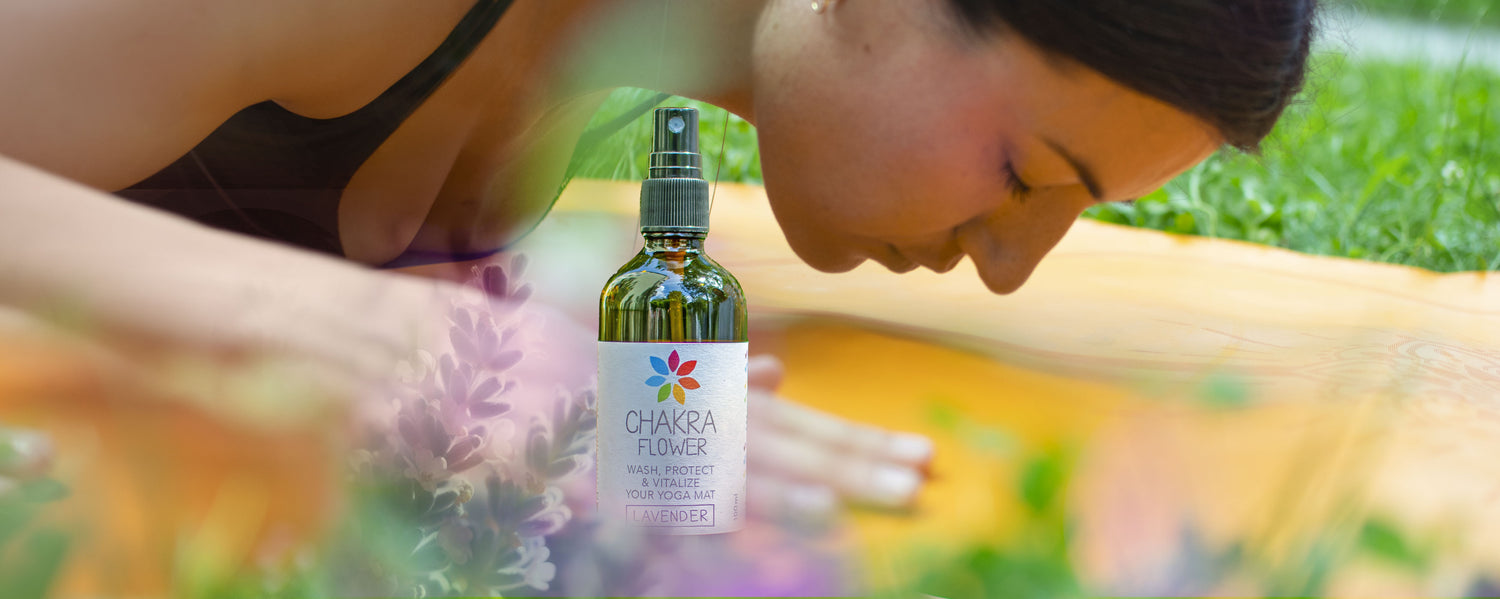 Eine Frau praktiziert Yoga auf einer Yogamatte inmitten einer natürlichen Umgebung. Neben ihr befinden sich Chakra Flower Yogamattenreiniger und andere Reinigungsprodukte. Das Bild verkörpert Ruhe, natürliche Reinigung und die Verbindung zwischen Mensch und Natur in der Yoga-Praxis